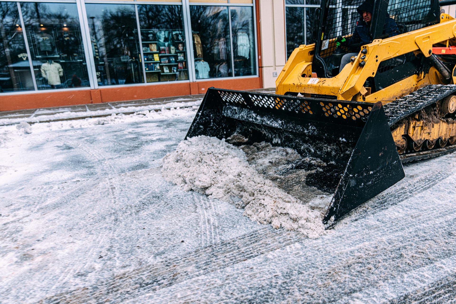 Man using a Bulldozer to remove snow and ice from a parking lot in Winter
